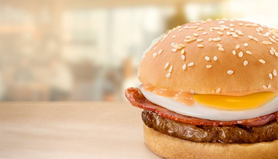 Breakfast bun with fried egg, bacon and beef patty on a toasted sesame seed bun