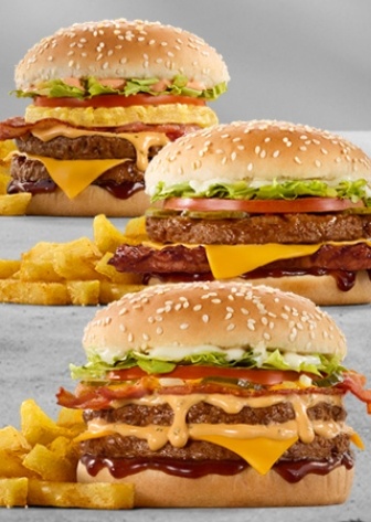 Three loaded bacon cheeseburgers with melted cheddar cheese, creamy sauce, lettuce, tomato, sesame seed buns, barbecue sauce, and chips