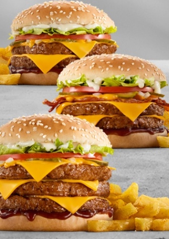 Three stacked cheeseburgers with double and triple beef patties, melted cheddar cheese, lettuce, tomato, pickles, sesame seed buns, barbecue sauce, and fries