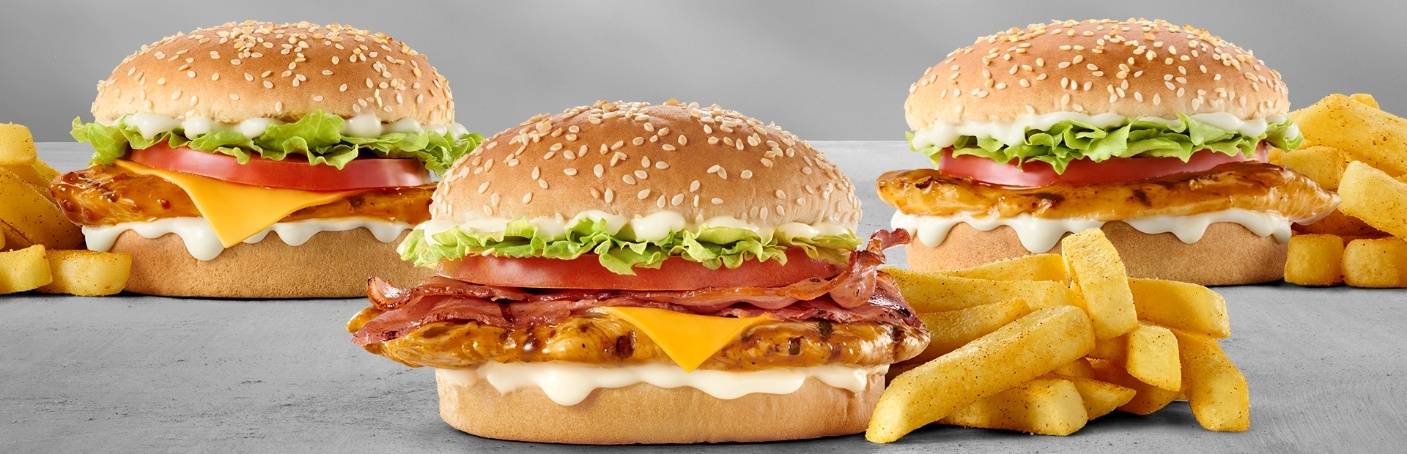 Three chicken cheeseburgers with grilled chicken fillets, crispy bacon, melted cheddar cheese, lettuce, tomato, creamy mayo sauce, sesame seed buns, and chips