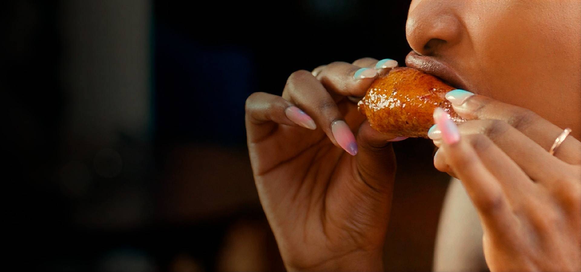 Person eating a glazed chicken wing with colorful acrylic nails, highlighting crispy fried chicken