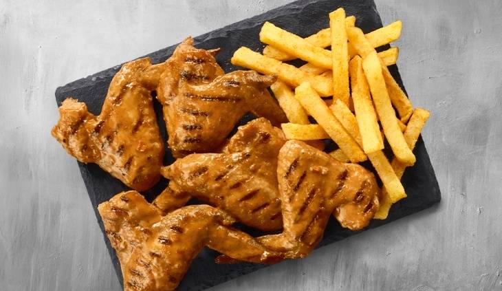 Grilled chicken leg quarters served with crispy seasoned chips on a black slate platter